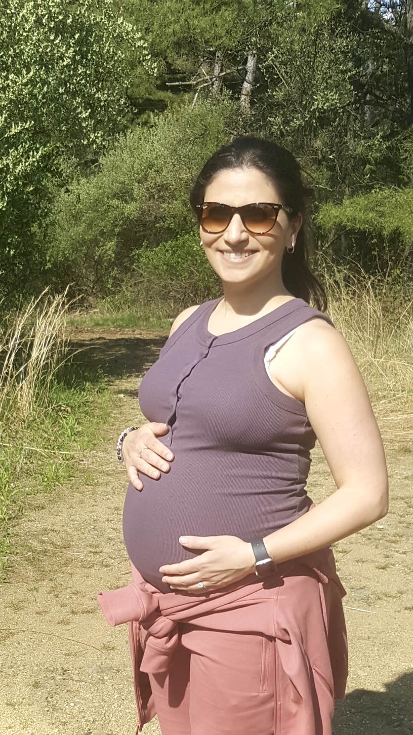 Pregnant mother standing on a sunlit nature trail with hands resting on her belly, reflecting on motherhood, healing, and new beginnings.