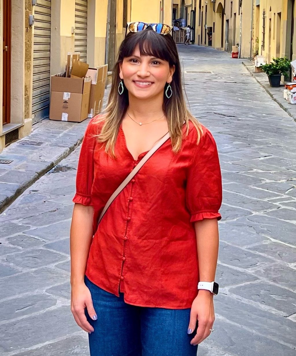 Melissa, author of Inspired Mama Blog, standing on a quiet street wearing a red blouse and smiling softly
